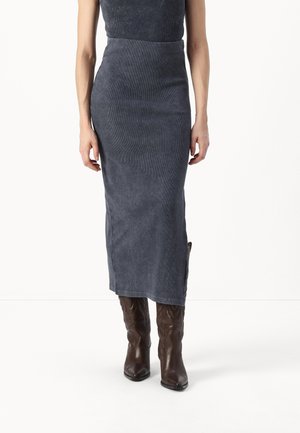 Jupe midi en velours côtelé bleu foncé avec une coupe ajustée, présentant une texture lisse et une silhouette droite, associée à des bottes de cowboy marron.