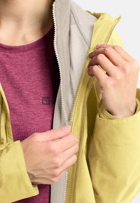 Geel waterdicht jack met een gestructureerde binnenvoering, gedeeltelijk open geritst. Een paarse shirt is zichtbaar eronder en toont een gladde stof.