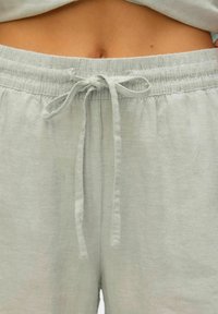 Lichtgroene shorts met elastische tailleband en een trekkoord. De stof heeft een zachte textuur en een relaxte pasvorm, met gathered stiksels aan de taille.