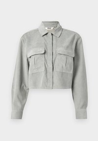 Camicia in velluto a coste grigia, tagliata, con colletto a punta e due taschini sul petto. Presenta maniche lunghe e un tessuto testurizzato.