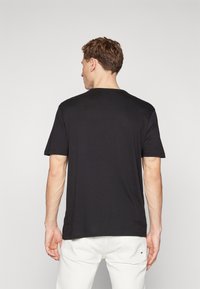 Maglietta nera in cotone a maniche corte, con colletto tondo e una texture liscia, presentata da dietro su uno sfondo neutro.