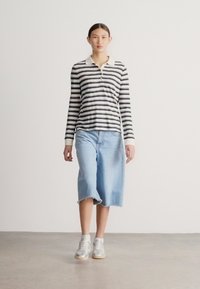 Tricou polo cu mâneci lungi cu dungi alb-negru, cu guler. Culottes din denim bleu deschis, cu tiv zdrențuit. Adidași gri cu talpă bej.