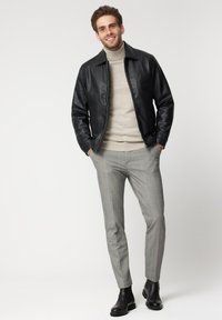 Czarna skórzana kurtka na beżowym golfie, połączona z szarymi spodniami w kratę i czarnymi botkami za kostkę. Czyste linie i dopasowany krój.