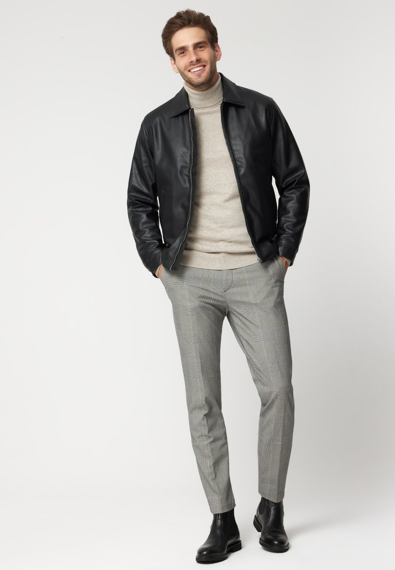 Czarna skórzana kurtka na beżowym golfie, połączona z szarymi spodniami w kratę i czarnymi botkami za kostkę. Czyste linie i dopasowany krój.