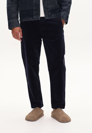 Marineblå kordfløjl bukser med en afslappet pasform og sidelommer, parret med brune ruskinds slip-on sko. Tekstureret stof synligt i lyset.