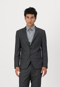 Veste de costume grise texturée avec un revers cranté, fermeture à un bouton et deux poches avant, associée à une chemise gris clair.