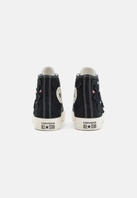 Czarne sneakersy wysokie ze wyszywanymi kwiatami, beżowymi gumowymi podeszwami, białymi szwami oraz okrągłą naszywką z logo na zewnętrznej pięcie.