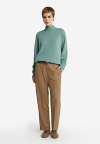 Jasnoniebieski, żebrowany sweter z golfem zestawiony z beżowymi, wysokim talią spodniami. Model nosi miękkie brązowe obuwie, ręce w kieszeniach.