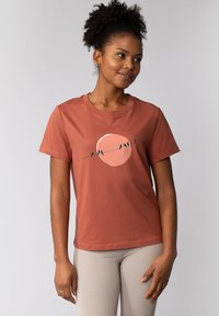 Rostfarbendes Baumwoll-T-Shirt mit kurzen Ärmeln, auf dem eine Grafik von einer Sonne und Vögeln auf einer feinen Linie über der Brust abgebildet ist.