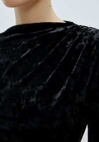 Schwarzes Samtkleid mit glatter Textur, verfügt über einen Bootsausschnitt und Falten an den Schultern für zusätzlichen Detailreichtum und Form.