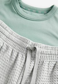Hellgrünes Baumwoll-T-Shirt kombiniert mit grauen, strukturierten Shorts mit elastischem Bund und Kordelzug.