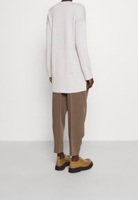 Ljusgrå oversized tröja med ribbat avslut, i kombination med lösa bruna byxor och bruna skor. Texturerna verkar mjuka och avkopplade.