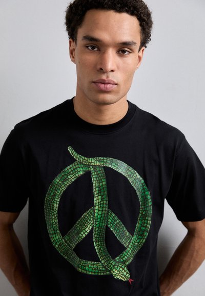 T-shirt en coton noir avec un grand serpent vert enlacé autour d'un symbole de paix. Une texture de scales vibrante et un détail de langue rouge sont remarquables.