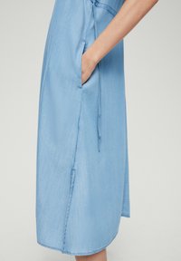 Jasnoniebieska sukienka z miękkiego materiału, z boczną kieszenią, prostym krojem i detalem w postaci sznureczka w talii.