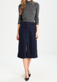 Námorně modrá áčková sukně z denimu s předním rozparkem a knoflíkovými detaily. Kombinováno s přiléhavým šedým pruhovaným topem s dlouhým rukávem a černými podpatky.