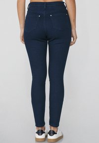 Jeans ajustados de color azul oscuro de mezclilla, con una cintura de altura media y bolsillos traseros. Combinados con zapatillas blancas con un acento negro.