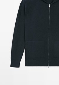 Granatowa bluza na zamek wykonana z miękkiej dzianiny, z dwoma przednimi kieszeniami i ściągaczami na rękawach dla lepszego dopasowania. Gładkie zapięcie na suwak.