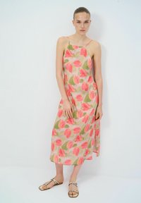 Bloemige midi-jurk met roze en groene tulp patronen op een lichte achtergrond, met dunne schouderbanden en een relaxte pasvorm. Platte sandalen.