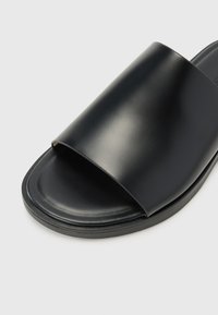 Black slide sandal featuring a smooth, matte finish with a wide upper strap and a cushioned sole. Simple design, no additional patterns or hardware.