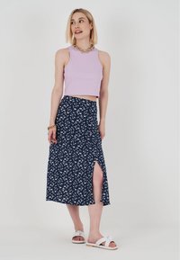 Lila ribbad croppad topp i kombination med en marinblå blommig midijirk som har en hög slits vid låret. Bärs med vita knutna sandaler och smycken i guldkedja.