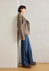 Bruine leren motorjack met zilveren ritssluiten, gecombineerd met wijde blauwe denim jeans en platform schoenen met panterprint.