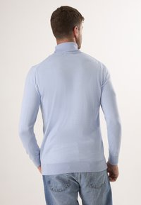 Lichtblauwe coltrui gemaakt van zachte brei stof, met lange mouwen en geribde manchetten en zoom. Draagt met blauwe spijkerbroek.