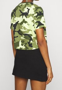 Camo krótka koszulka w zielone i czarne wzory, wykonana z miękkiej bawełny, zestawiona z teksturowaną, krótką czarną spódnicą.