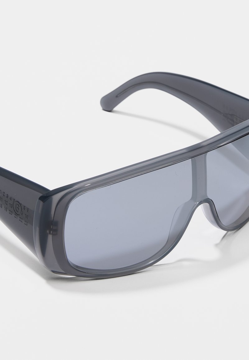 Sunglasses with a gray translucent frame and large, dark tinted lenses. Designed with smooth edges and curved arms for secure fit.