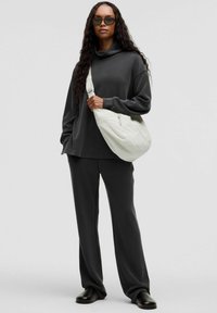 Mørkegrå oversized sweatshirt med cowl-neck og matchende bukser, suppleret med en hvid slouchy taske og sorte sko.