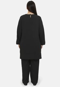 Sort, langærmet tunika med en lille nøglehulbag på ryggen og brede, løstsiddende bukser lavet af blødt stof med et enkelt design.