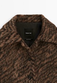Manteau en laine à motifs brun et noir avec une finition texturée, col cranté et deux boutons noirs. Présente une étiquette cousue à l'intérieur.