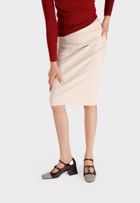 Zapatos de tacón alto con acabado de charol. Presentan una parte superior marrón con una puntera de color verde olivo y una correa con hebilla alrededor del tobillo.