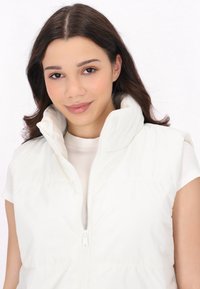 Gilet smanicato bianco in materiale imbottito, con colletto alto e chiusura a zip, caratterizzato da cuciture orizzontali e una texture liscia e lucida.