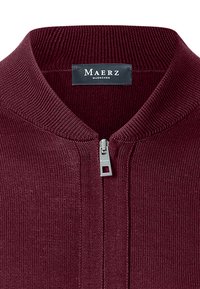 Maglione in maglia bordeaux con colletto alto e zip argentata. Il tessuto ha una finitura texture, e l'etichetta reca la scritta "Maerz Muenchen."