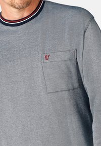 Grijs longsleeve shirt met een ronde hals en een marineblauwe en rode gestreepte kraag. Inclusief een borstzak aan de linkerzijde met rode logodetail.