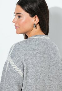 Grå stickad tröja med en texturerad yta och ljusare grå horisontella ränder längs axelsömmarna. Har en rund halsringning.