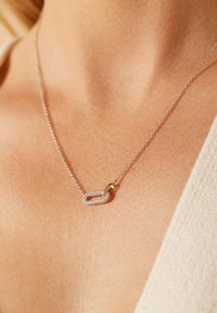 Zilveren ketting met een rechthoekige hanger met een gouden accent, versierd met kleine sprankelende stenen.