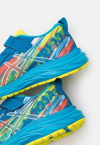 Scarpe atletiche blu con tomaia strutturata decorata da vivaci motivi gialli, arancioni e verdi. Cinghia in velcro e dettagli prominenti della suola.