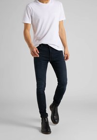 Camiseta blanca de cuello redondo combinada con jeans ajustados de color azul oscuro y botas negras hasta el tobillo, con una textura suave y un diseño simple.