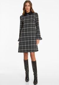Black and gray plaid dress with long sleeves, flared cuffs, and a high collar featuring black accents. Model wears knee-high, shiny black boots.