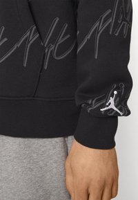 Schwarzer Sweatshirt mit einem grafischen Design und dem Jordan-Logo auf dem Ärmel. Das Material besteht aus einem weichen Baumwollgemisch mit gerippten Bündchen.