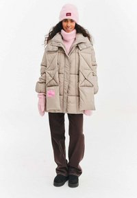Beżowy pikowany płaszcz z przeszyciami w kształcie diamentu, różowymi akcentami, zatrzaskami, warstwowym kołnierzem, różowymi rękawiczkami, ciemnobrązowymi spodniami i czarnymi butami.
