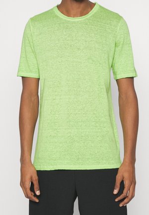 Mand iført en lysegrøn kortærmet T-shirt med rund hals og sorte bukser, vist fra skuldre til hofter mod hvid baggrund.