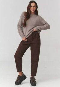 Jasnobrązowy sweter z dzianiny o luźnym kroju, w zestawieniu z ciemnobrązowymi spodniami o wysokim stanie. Masywne czarne buty z sznurowadłami.