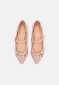 Ballerines Mary Jane en cuir verni rose avec bout pointu, bride cheville et détail de chaîne dorée sur le devant. Texture lisse et design minimaliste.