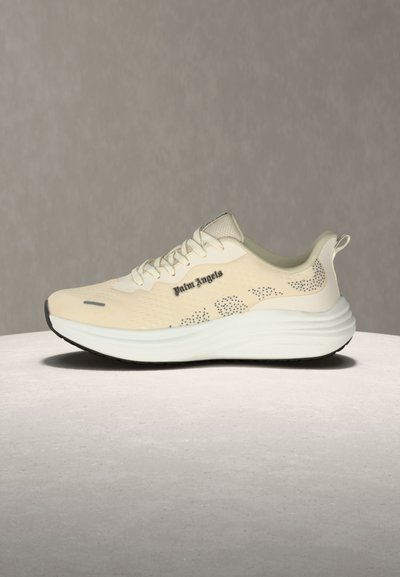 Μπεζ sneaker Palm Angels με λευκή χοντρή σόλα, τρυπητές λεπτομέρειες στα πλάγια και κορδόνια σε γκρι επιφάνεια και φόντο.