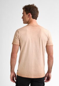 Béžové bavlněné tričko s krátkým rukávem, kulatým výstřihem, jemnou texturou a čistým zakončením na spodním lemu. Zobrazeno zezadu.
