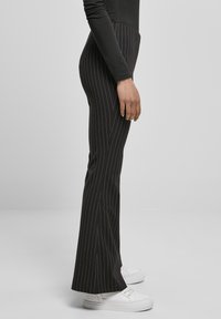 Mustad triibulised laiade säärega püksid, millel on sile tekstuur, kõrge vöökoht ja kontrastsed valged triibud, kantud valgete tennistega.