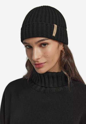 Black ribbed knit beanie with a folded cuff and a small light brown tag. Soft texture, fitted design, suitable for cold weather.