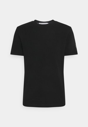 Czarny krótki rękaw T-shirt wykonany z miękkiej bawełny. Posiada okrągły dekolt oraz subtelny detal logo na lewym rękawie. Gładka tekstura.